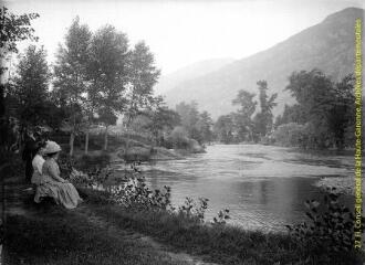 Groupe assis au bord de l'eau dans un paysage de montagne. - [entre 1900 et 1920]. - Photographie