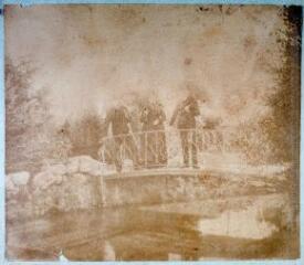 Photographie de trois personnes sur le petit pont du parc de l'usine Brusson. Les trois personnes dont une femme et deux hommes portent chacun une ombrelle.