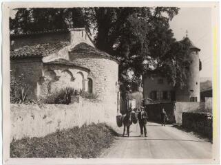 Hameau de Vic d'Oust (Oust, Ariège) : église (absides romanes, côté est) et rue animée du village (un homme et son âne) / J.-E. Auclair photogr. - [entre 1920 et 1950]. - Photographie