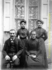 1 vue - Portrait de famille en extérieur devant la maison (avec deux jeunes femmes portant une robe imprimée à petits pois). - [entre 1900 et 1920]. - Photographie (ouvre la visionneuse)