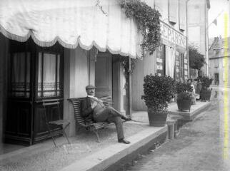 1 vue - Cierp-Gaud : homme assis en pose sur un banc devant le café-restaurant Abadie (place de la Toucouere). - [entre 1900 et 1920]. - Photographie (ouvre la visionneuse)