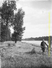 1 vue - Un homme en pose avec sa bicyclette près d\'un cours d\'eau. - [entre 1900 et 1920]. - Photographie (ouvre la visionneuse)