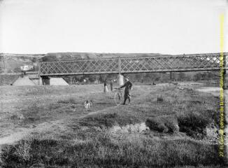 1 vue - Un homme en pose avec sa bicyclette près d\'un cours d\'eau, avec un pont en arrière plan. - [entre 1900 et 1920]. - Photographie (ouvre la visionneuse)