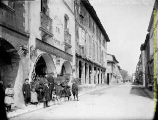 1 vue - Saint-Sulpice-sur-Lèze : hommes et enfants devant un café dans une rue avec passages couverts. - [entre 1900 et 1920]. - Photographie (ouvre la visionneuse)