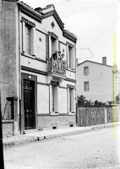 1 vue - Façade de maison en bord de rue : balcon, fronton triangulaire et enseigne \'Robes\'. - [entre 1900 et 1920]. - Photographie (ouvre la visionneuse)