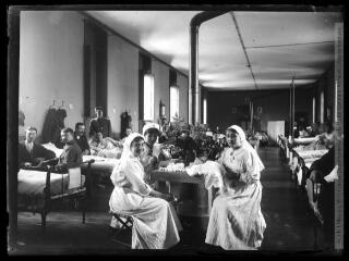 1 vue  - Hôpital temporaire n° 23 : dans une chambre commune, trois infirmières et les lits occupés. - 1915-1916. - Photographie (ouvre la visionneuse)