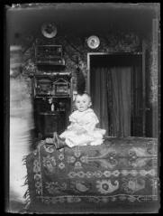 1 vue  - Portrait en intérieur d\'un enfant en bas âge assis sur un tapis. - [entre 1890 et 1920]. - Photographie (ouvre la visionneuse)