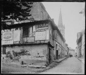 1 vue - [Muret : rue dans le quartier de l\'église Saint-Jacques, avec une façade d\'enseignes publicitaires]. - [1925 ?]. - Photographie (ouvre la visionneuse)