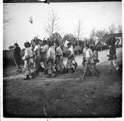 1 vue Les militaires en uniforme blanc marchent, encadrés par des officiers.