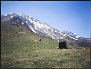 2 vues Un versant avec restes de neige et cabanes en bois, ruches.