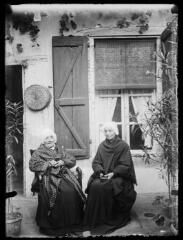1 vue Portrait de deux femmes âgées assises devant une maison (coiffe, châle). - Photographie