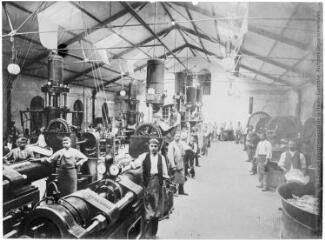 1 vue Salle de fabrication, ou galerie des machines, à gauche, les presses, à droite les pétrins à meules verticales, les employés posent devant l'objectif à côté des machines.