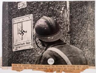 2 vues Sur le front français. Dans un village occupé par nos troupes un soldat regarde l'écriteau du siège de la Ligue coloniale allemande / photographie Agence Trampus, Paris. - 13 octobre 1939. - Photographie